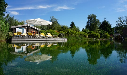 Naturbadesee neben Holzhütte und Liegen
