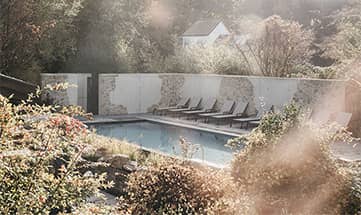 Blick durch die Natur auf den Außenpool und die Liegen