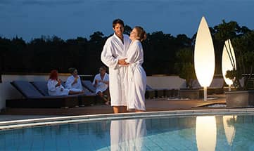 Paar in weißen Bademäntel neben dem Pool am Abend