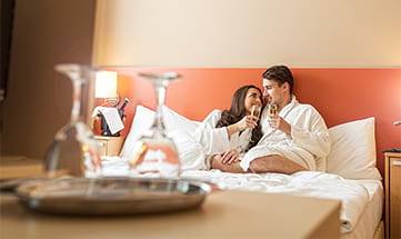 Paar in weißen Bademänteln entspannt mit Sekt auf Bett